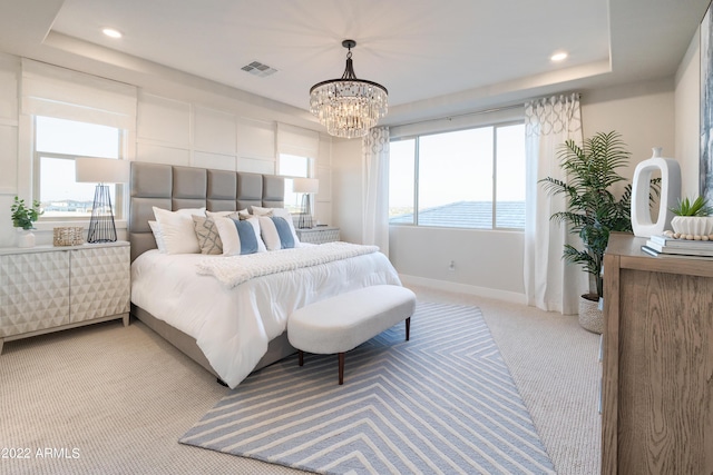 bedroom with a raised ceiling, light colored carpet, and a notable chandelier
