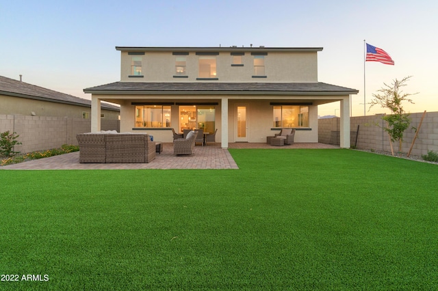 back house at dusk featuring an outdoor living space, a patio area, and a lawn
