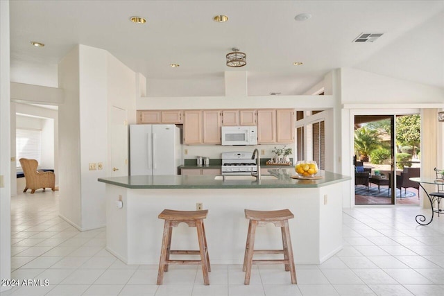 kitchen featuring light brown cabinets, a kitchen island with sink, lofted ceiling, and white appliances