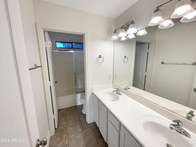 full bathroom with double sink, tile floors, toilet, large vanity, and enclosed tub / shower combo