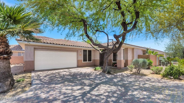 ranch-style home with concrete driveway, an attached garage, a tile roof, and stucco siding