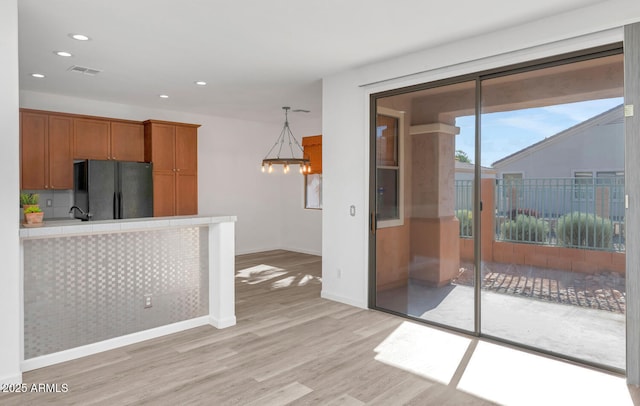 kitchen with visible vents, light countertops, light wood-style flooring, freestanding refrigerator, and brown cabinetry