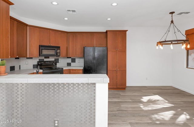 kitchen featuring visible vents, black appliances, light wood-style flooring, tile countertops, and a peninsula