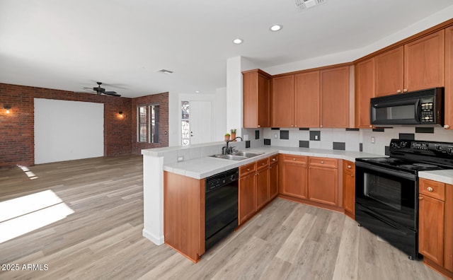 kitchen with black appliances, light wood-style flooring, a peninsula, and a sink