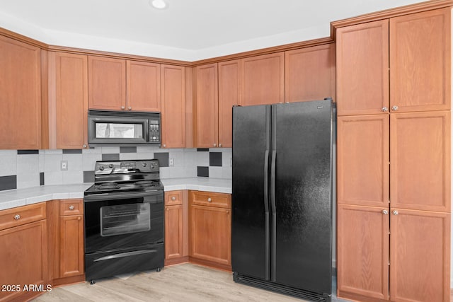 kitchen with black appliances, light wood-style flooring, tile countertops, brown cabinetry, and decorative backsplash