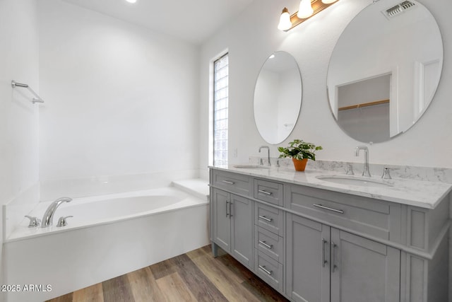 full bath featuring a sink, visible vents, a garden tub, and wood finished floors