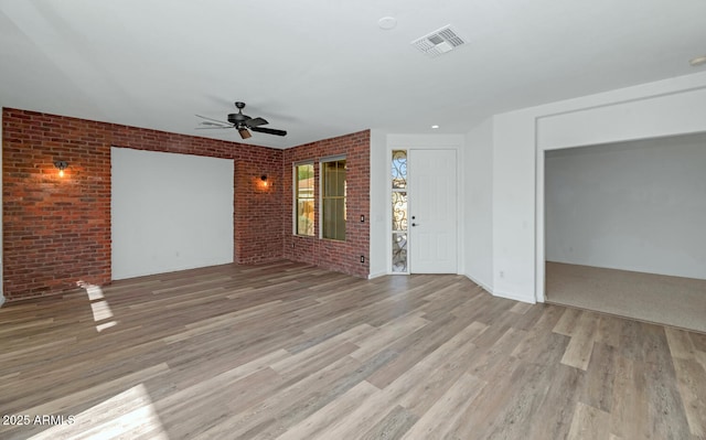 unfurnished living room with ceiling fan, visible vents, brick wall, and light wood finished floors