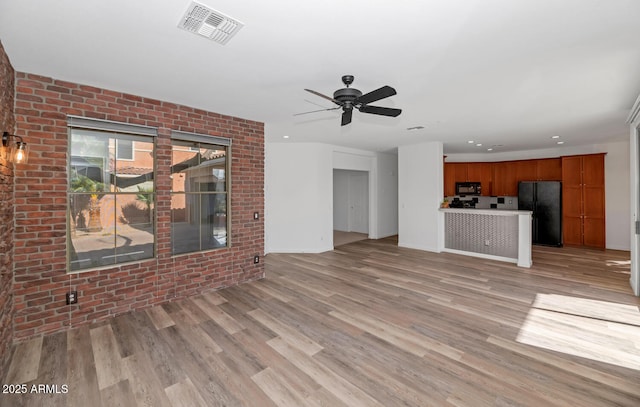 unfurnished living room featuring light wood-type flooring, visible vents, brick wall, and a ceiling fan