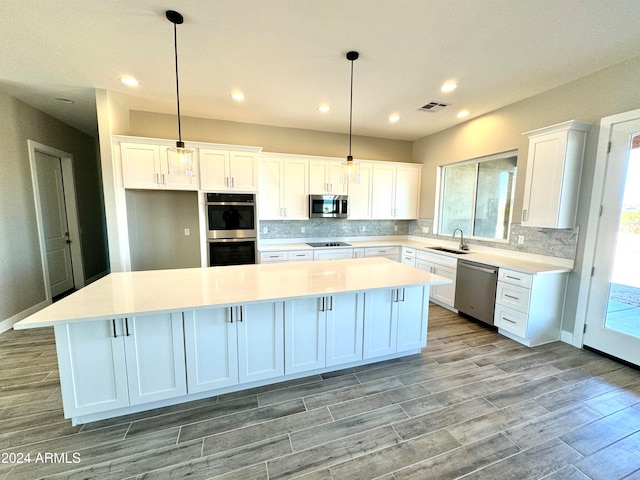 kitchen featuring stainless steel appliances, light hardwood / wood-style flooring, white cabinets, a center island, and hanging light fixtures