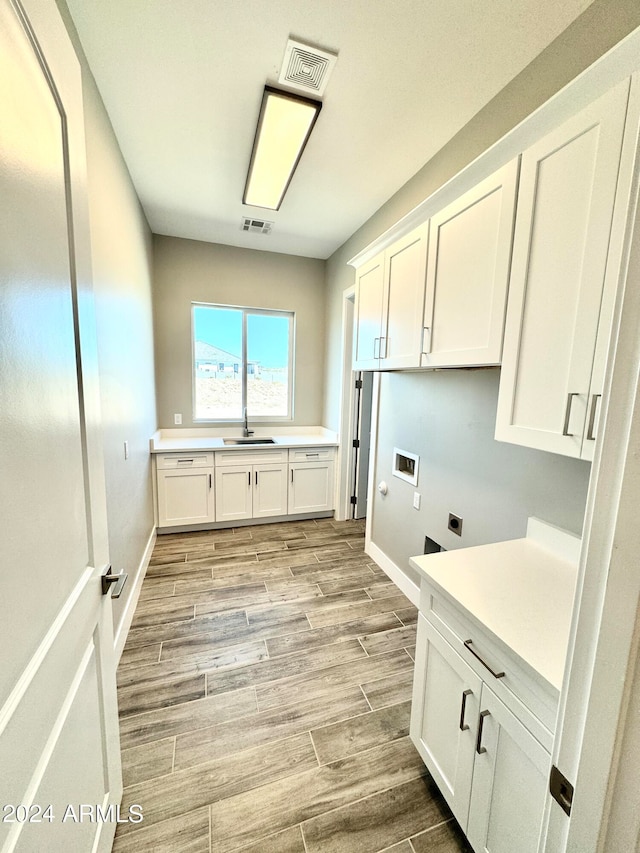 clothes washing area featuring electric dryer hookup, cabinets, sink, hookup for a washing machine, and light hardwood / wood-style flooring