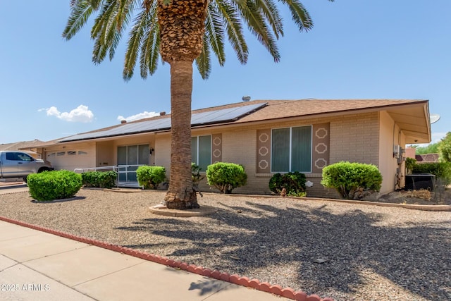 ranch-style house with solar panels, central AC unit, and a garage