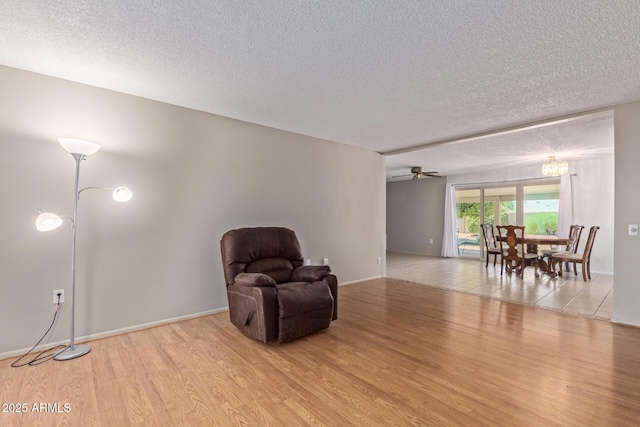 living area with ceiling fan with notable chandelier, a textured ceiling, and light hardwood / wood-style floors