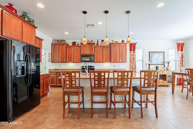 kitchen with an island with sink, a breakfast bar, pendant lighting, and black appliances