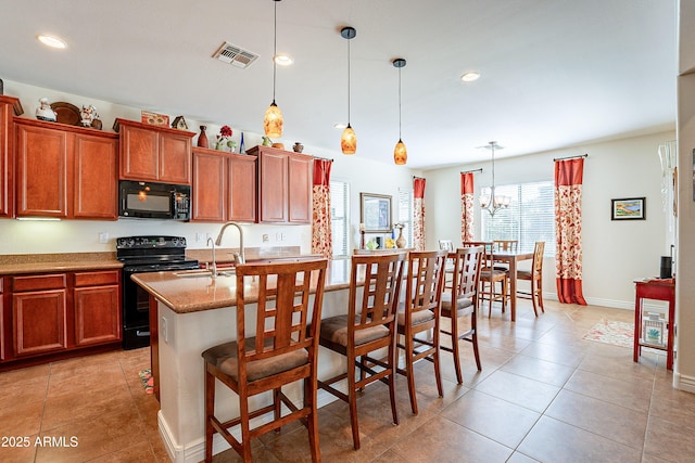 kitchen featuring a breakfast bar, sink, decorative light fixtures, a kitchen island with sink, and black appliances