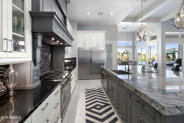 kitchen with sink, white cabinets, a chandelier, premium appliances, and dark stone counters