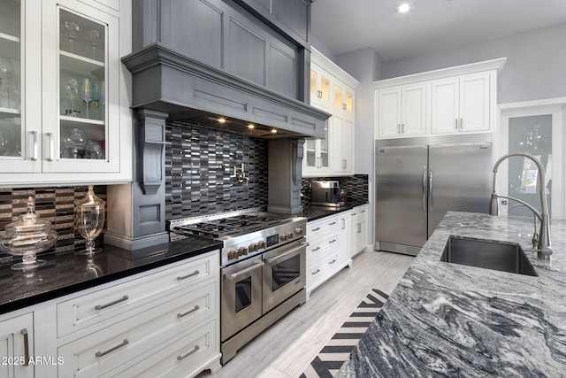 kitchen with sink, high end appliances, white cabinetry, tasteful backsplash, and dark stone counters