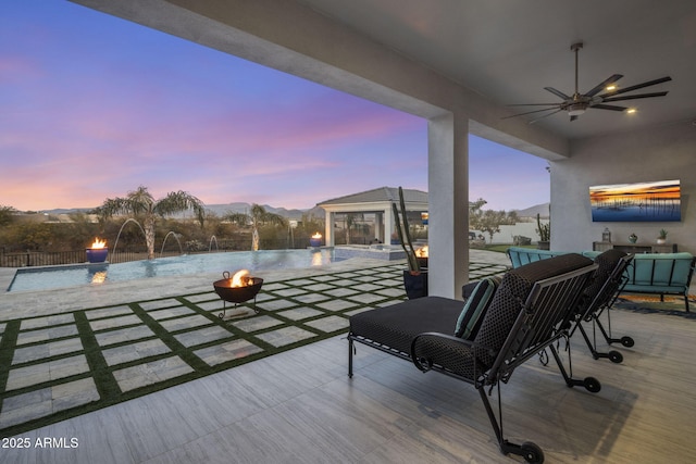 patio terrace at dusk featuring pool water feature, an outdoor fire pit, and a mountain view