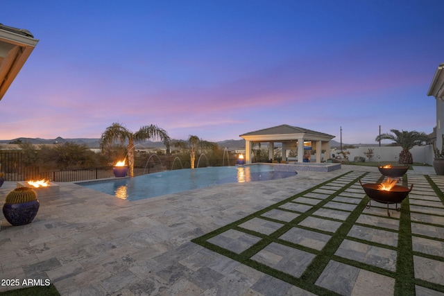 pool at dusk featuring a patio, a gazebo, pool water feature, and an outdoor fire pit