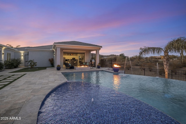 pool at dusk featuring pool water feature and a patio