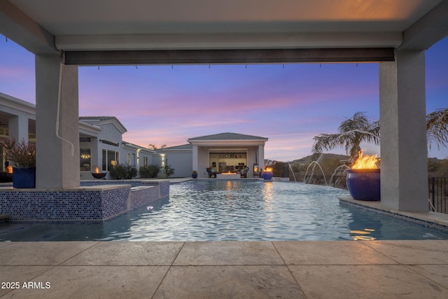 pool at dusk featuring pool water feature and an in ground hot tub