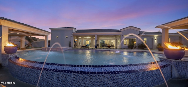 pool at dusk with a patio, pool water feature, and an outdoor fire pit