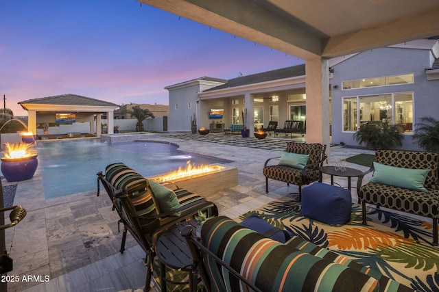 pool at dusk featuring a patio, pool water feature, a gazebo, and an outdoor living space with a fire pit