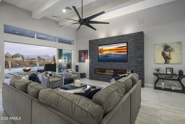 living room with ceiling fan, a high ceiling, a mountain view, a stone fireplace, and beamed ceiling