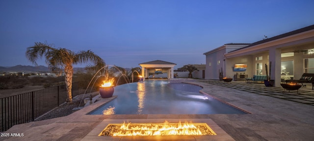 pool at dusk featuring a gazebo, pool water feature, a patio, and a fire pit