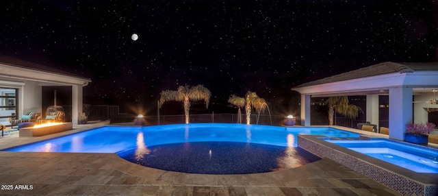 pool at night with a fire pit, a patio, and an in ground hot tub