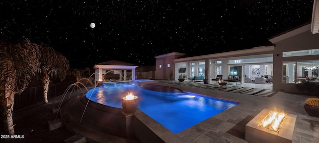 pool at night featuring a gazebo, pool water feature, an outdoor living space with a fire pit, and a patio area