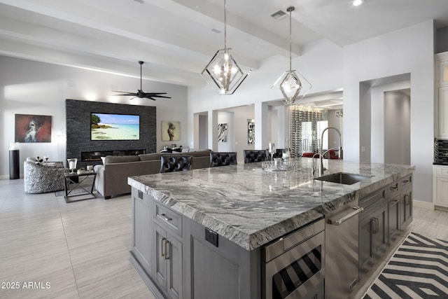 kitchen featuring sink, dark stone countertops, stainless steel microwave, a center island with sink, and decorative light fixtures