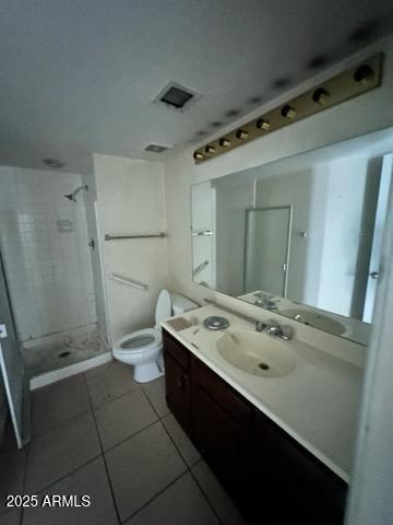 bathroom featuring tile patterned flooring, toilet, vanity, and tiled shower