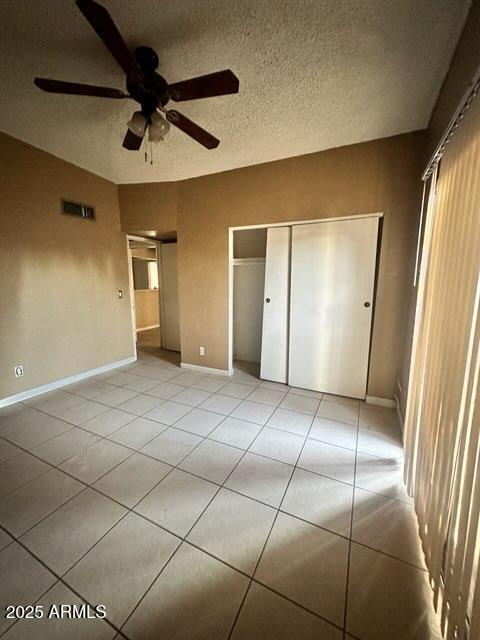 unfurnished bedroom featuring ceiling fan, light tile patterned floors, a textured ceiling, and a closet