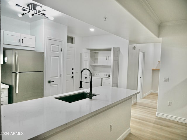 kitchen featuring white cabinetry, washing machine and clothes dryer, stainless steel refrigerator, light hardwood / wood-style floors, and sink