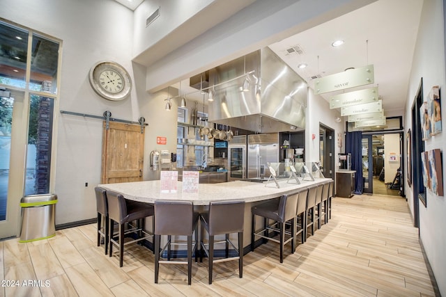 kitchen featuring a kitchen bar, light stone counters, a barn door, and light hardwood / wood-style flooring