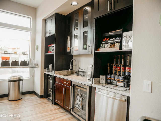 bar featuring light hardwood / wood-style flooring, sink, light stone countertops, beverage cooler, and stainless steel dishwasher