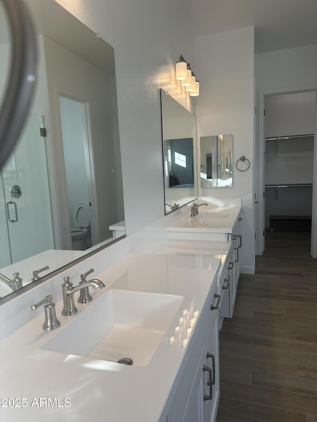 bathroom featuring double vanity, a spacious closet, wood finished floors, and a sink