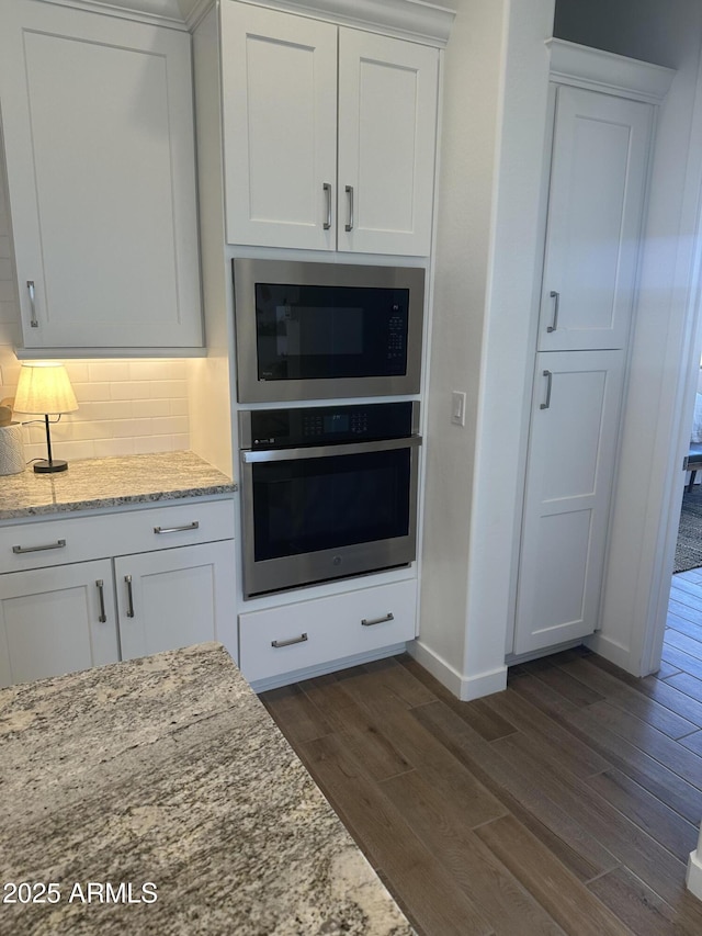 kitchen with tasteful backsplash, white cabinets, stainless steel oven, built in microwave, and dark wood-style flooring