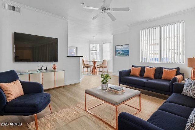 living room featuring light wood finished floors, visible vents, baseboards, a ceiling fan, and crown molding