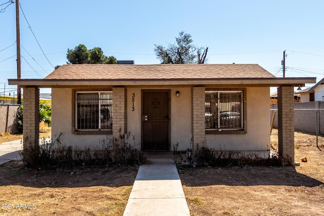 bungalow-style house featuring stucco siding, roof with shingles, and fence