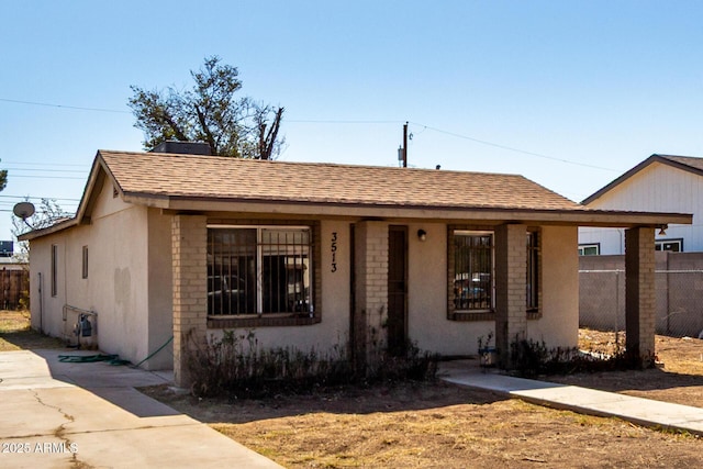 view of front facade featuring stucco siding, roof with shingles, and fence