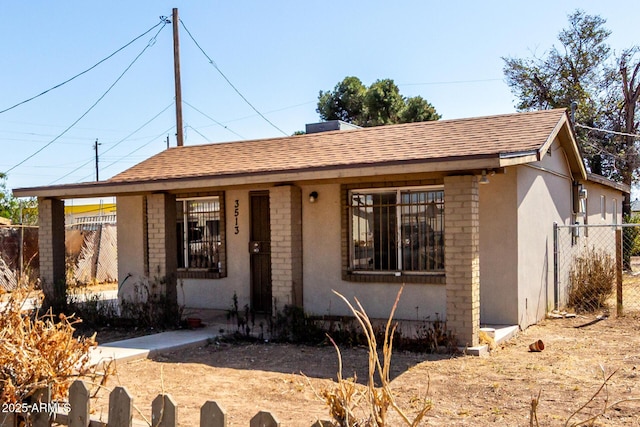 view of front facade featuring a shingled roof, fence, and stucco siding