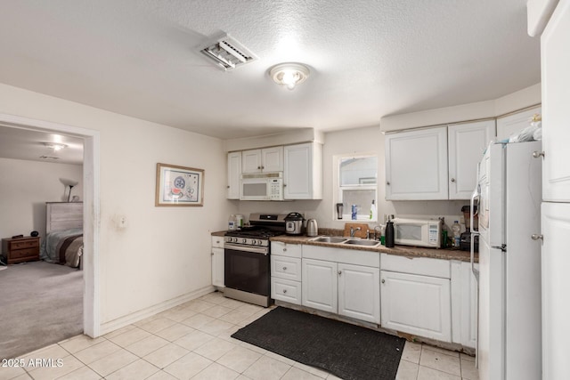 kitchen featuring dark countertops, visible vents, white cabinets, white appliances, and a sink