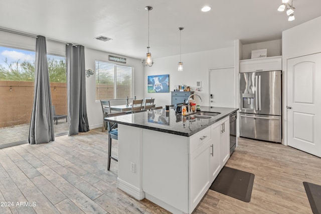 kitchen with white cabinetry, sink, stainless steel fridge, and an island with sink