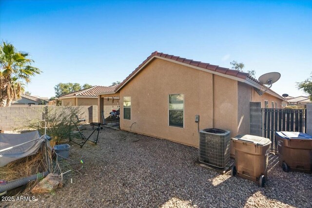 rear view of house with fence, stucco siding, central AC, and a tiled roof
