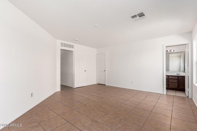 unfurnished bedroom with baseboards, connected bathroom, light tile patterned flooring, and visible vents