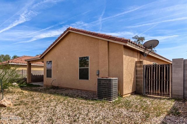 view of home's exterior featuring a tiled roof, central AC unit, a gate, fence, and stucco siding