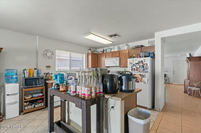 kitchen with brown cabinets, white appliances, a textured ceiling, light tile patterned floors, and visible vents