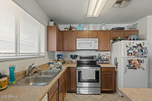 kitchen featuring visible vents, white appliances, light countertops, a sink, and light tile patterned floors