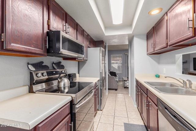 kitchen featuring a tray ceiling, light tile patterned floors, stainless steel appliances, light countertops, and a sink